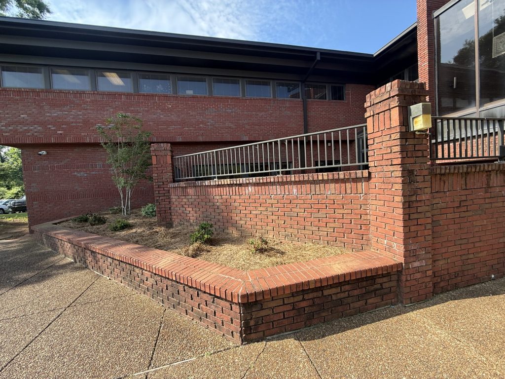 Brick retaining wall before cleaning, with dark growth on the lower wall, at Hospice Family Care in Huntsville, AL